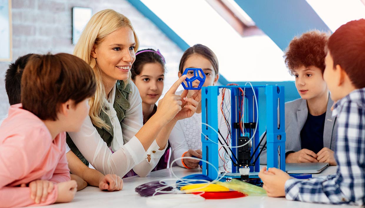 woman holding up a learning tool teaching a group of young children in a classroom environment.