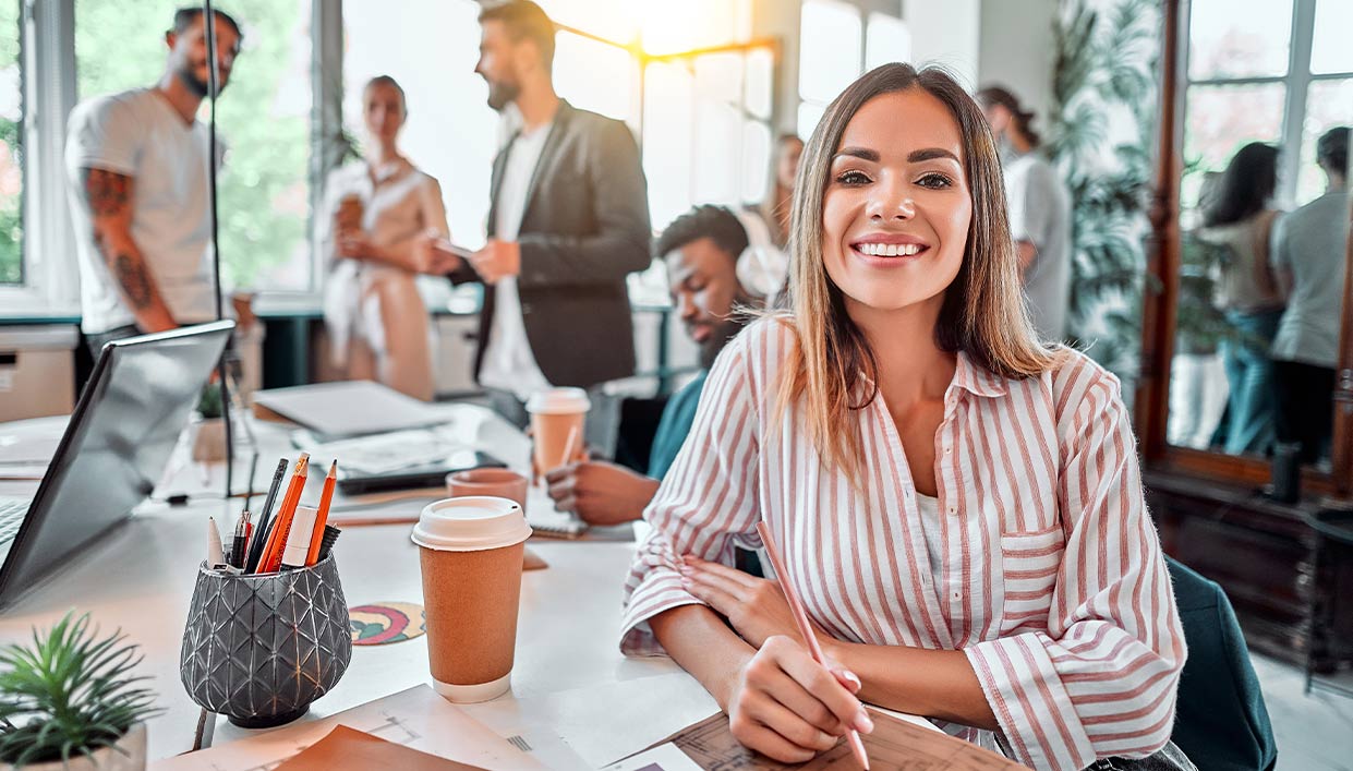 Business professional woman smiling sitting at a desk in a casual office setting.